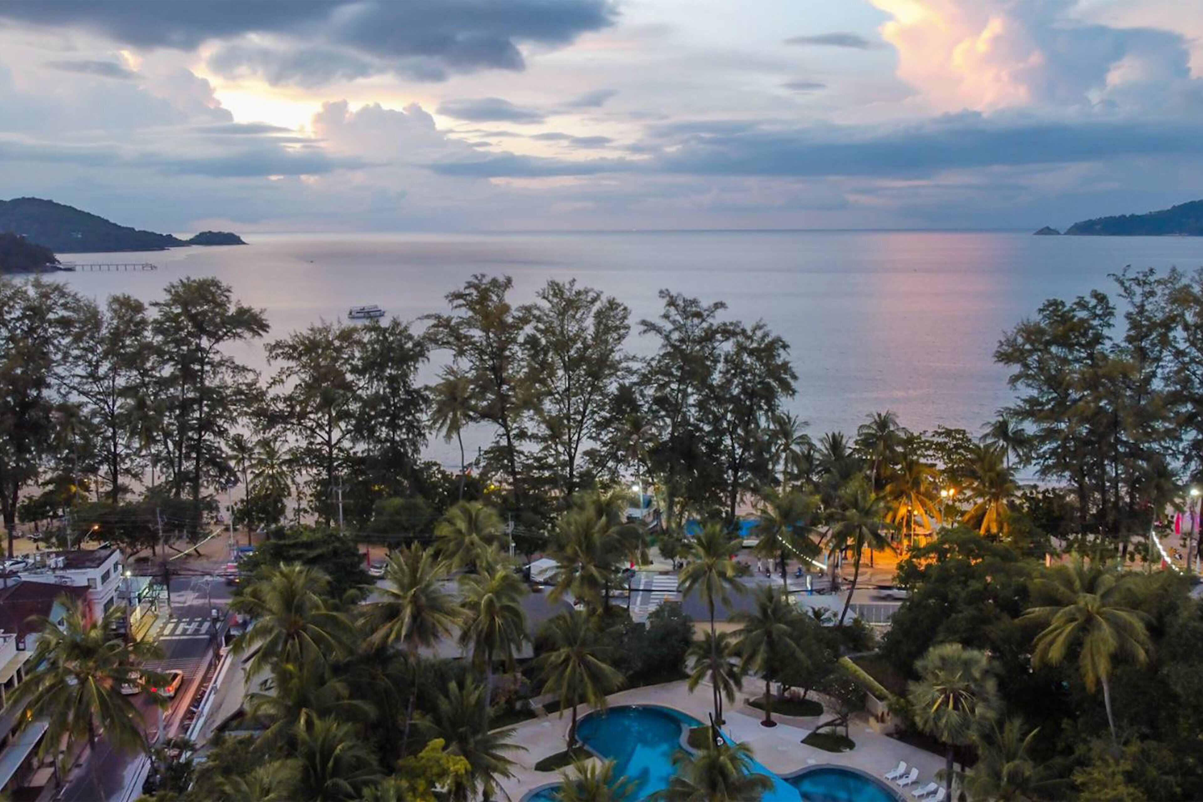 A resort with a pool, palm trees, and a view of the sea.