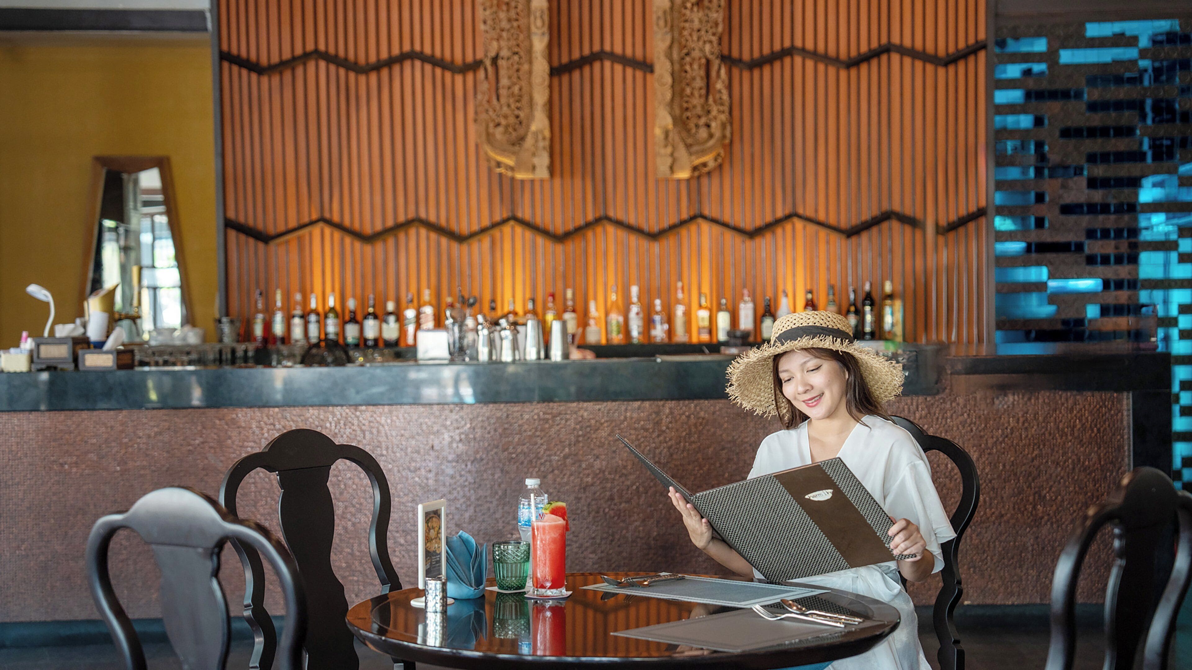 Eine Person sitzt an einem Tisch in einem Restaurant, im Hintergrund ist eine Bar zu sehen.
