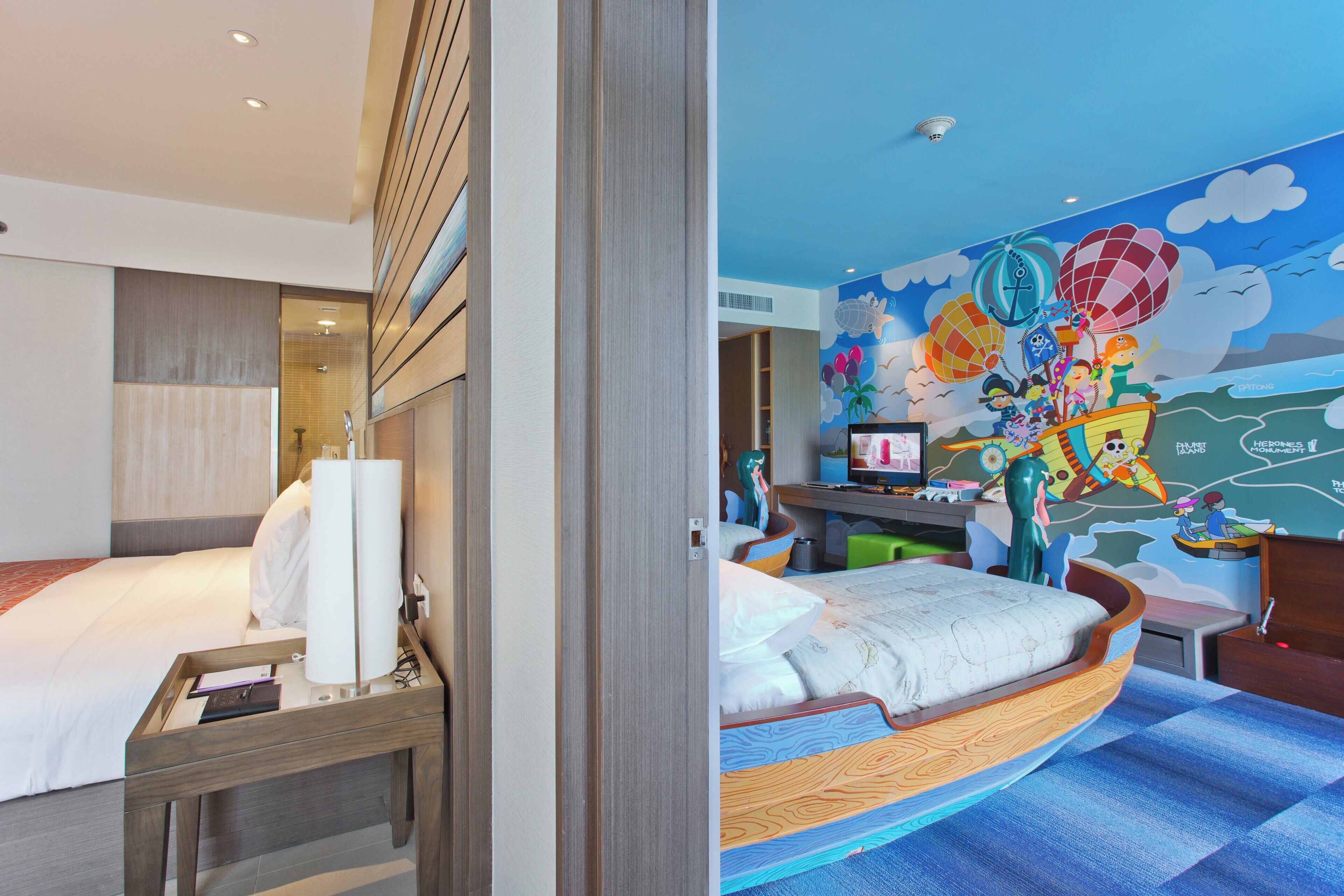 Una habitación de hotel con cama, escritorio, computadora y un mural colorido en la pared.