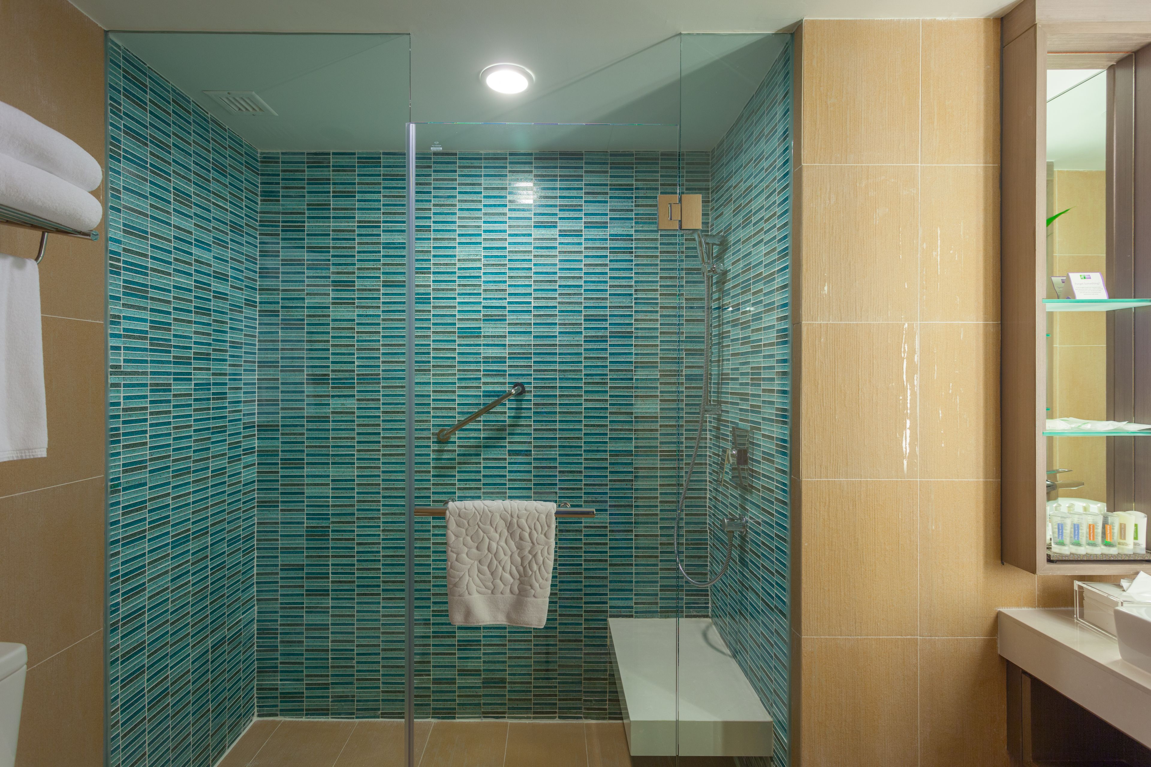 A modern bathroom with a glass-enclosed shower, a white towel hanging on a rack, and a mirror with toiletries.