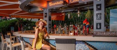 A bar area with a neon sign, a variety of bottles, and a parrot decoration.