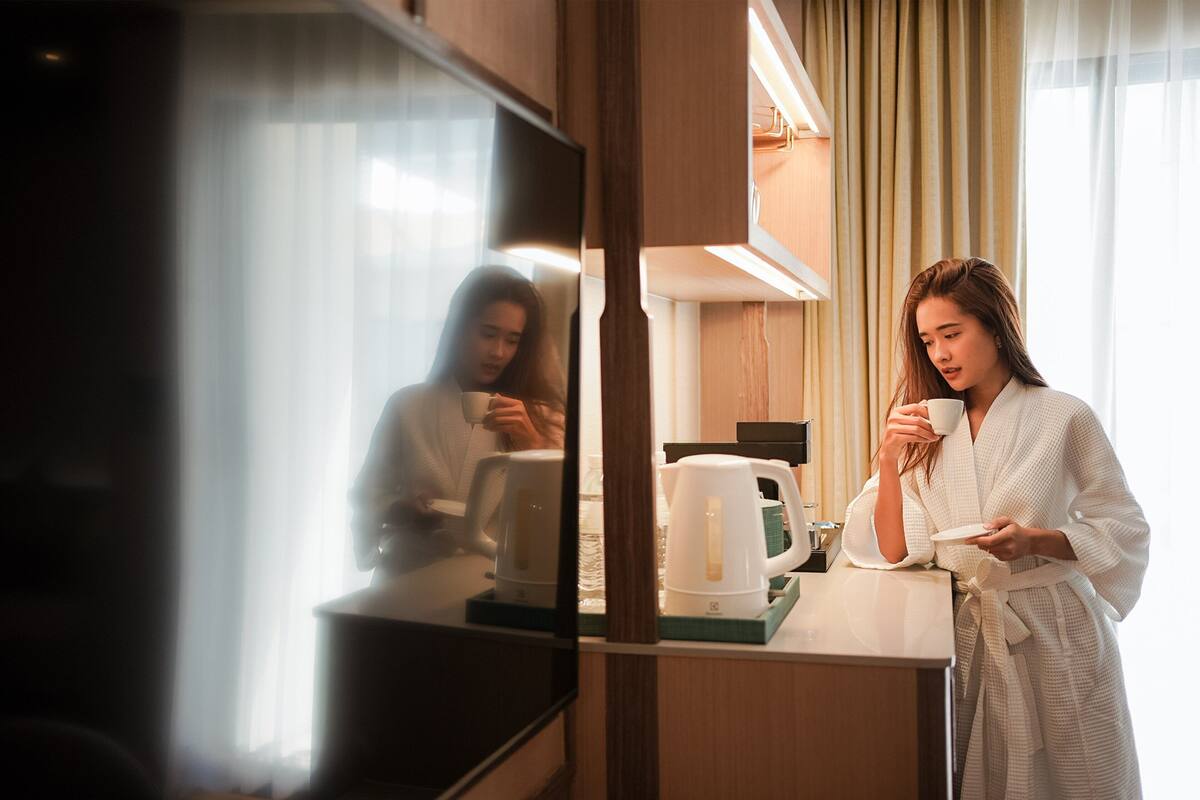 A hotel room with a kitchen area, a television, and a large mirror reflecting the room.