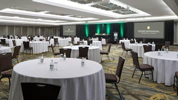 Una sala de conferencias con varias mesas redondas, sillas y un escenario con una pantalla que muestra el logo del InterContinental Toronto Centre.