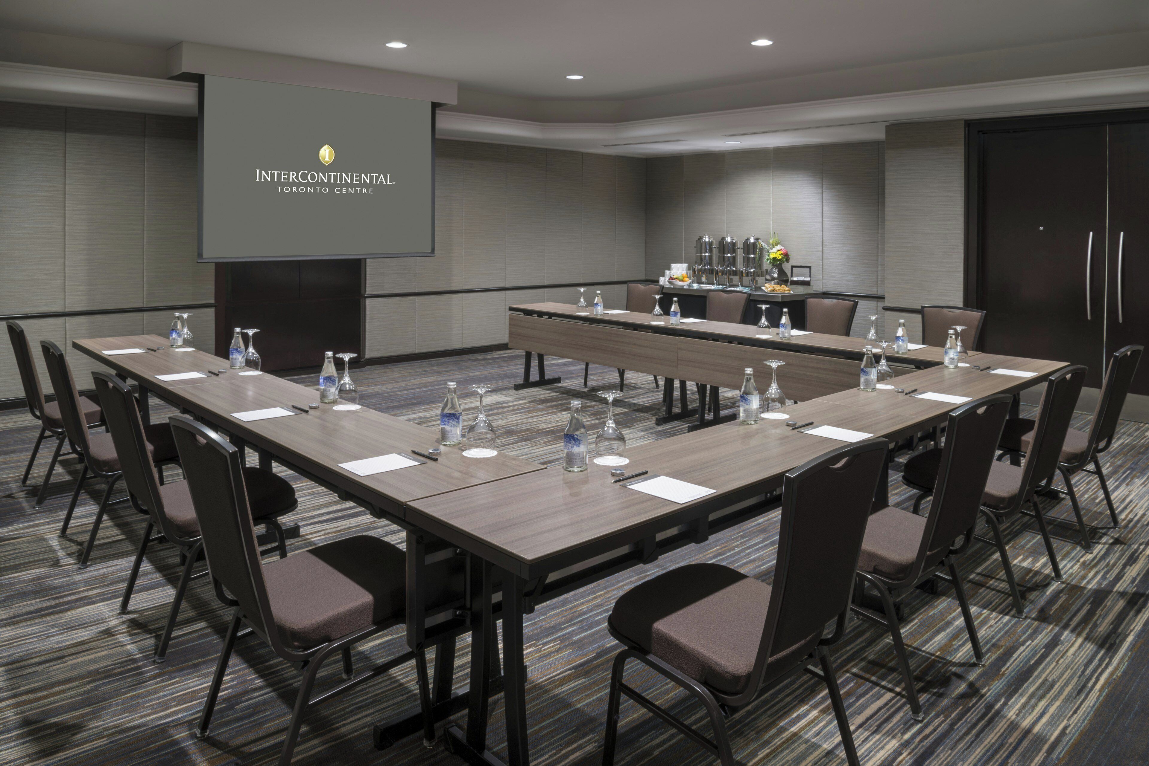 Un salón de conferencias con una larga mesa, sillas, una pantalla de proyector y un refrigerador.