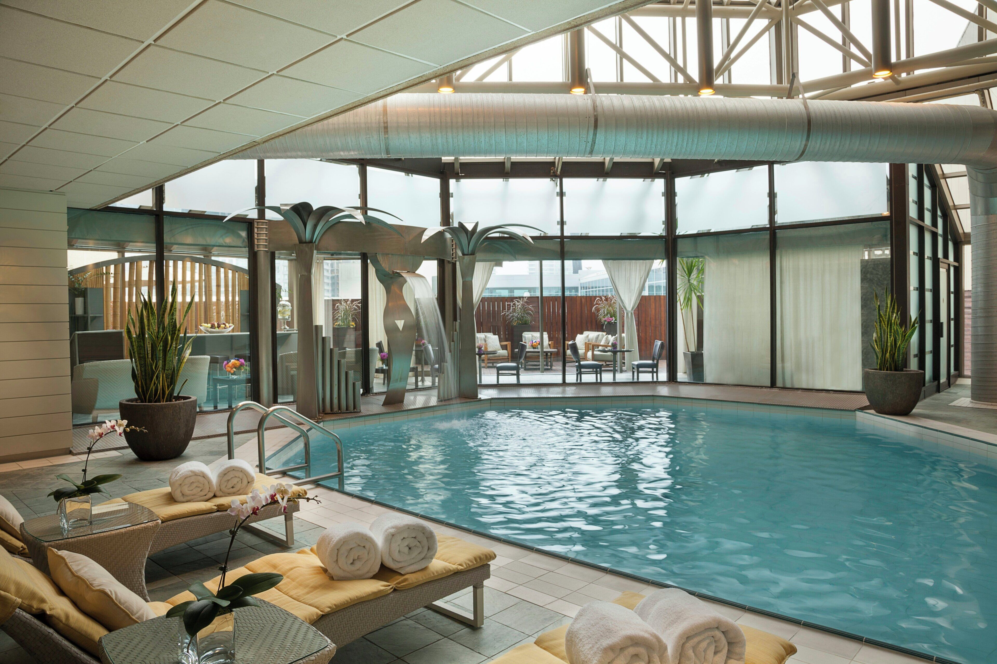 An indoor swimming pool with lounge chairs, towels, and potted plants.