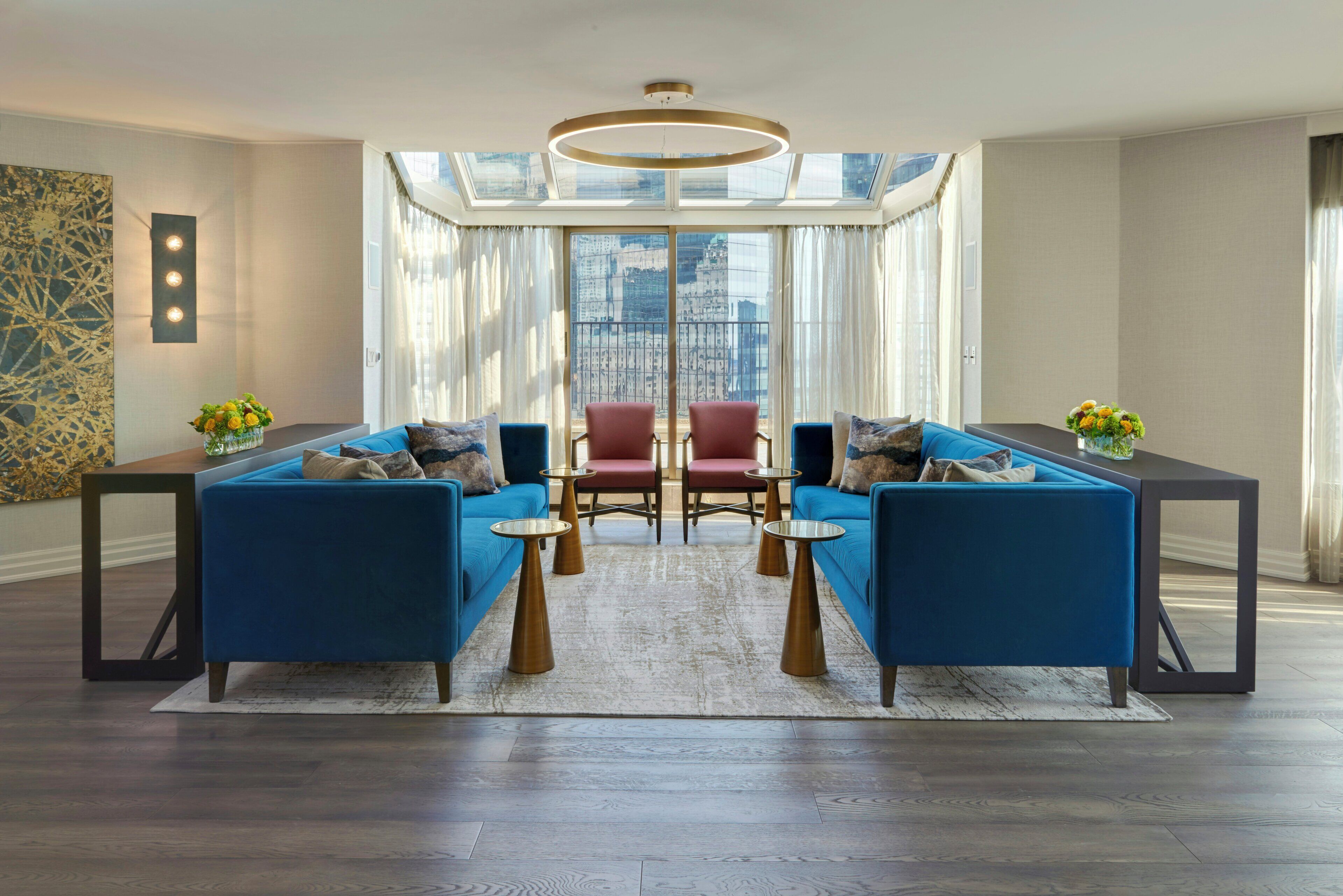 Una sala moderna con sofás azules, un sillón rojo central y una mesa de centro de vidrio.