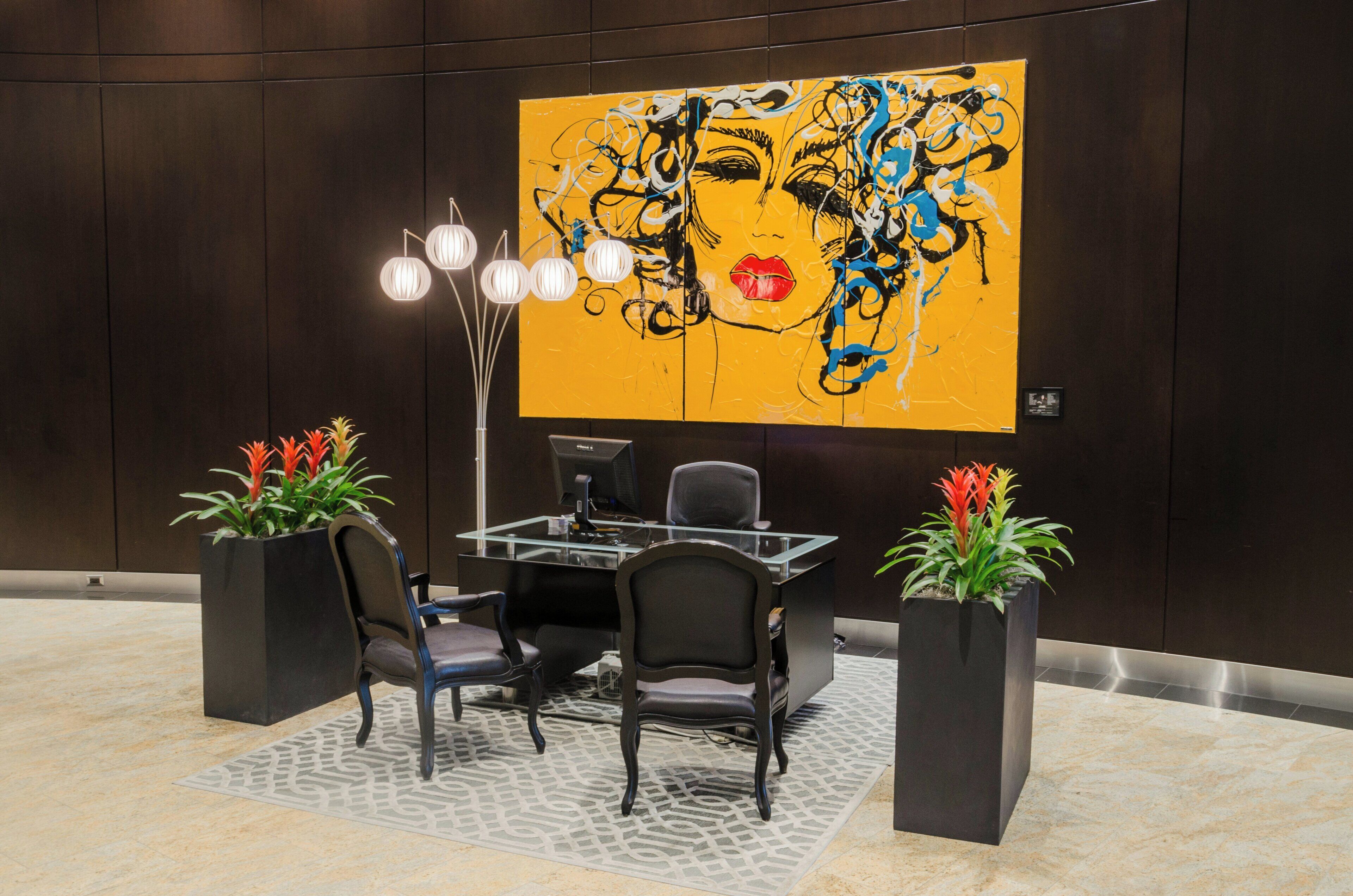 A modern office space with a large abstract painting, a glass table, and two potted plants.