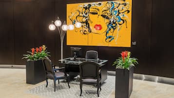 A modern office space with a large abstract painting, a glass table, and two potted plants.