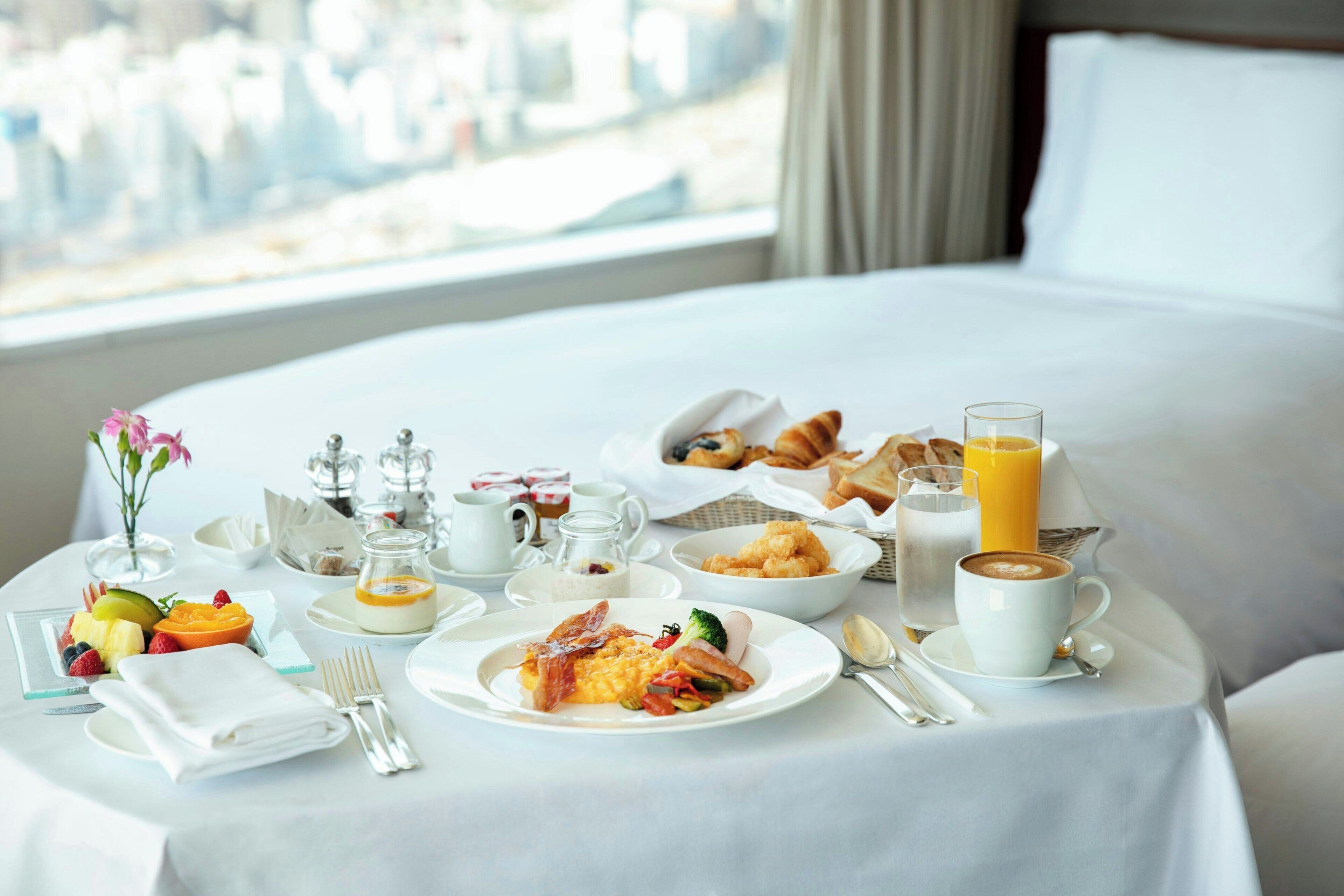 A breakfast setup on a bed with various food items, a glass of orange juice, and a cup of coffee.