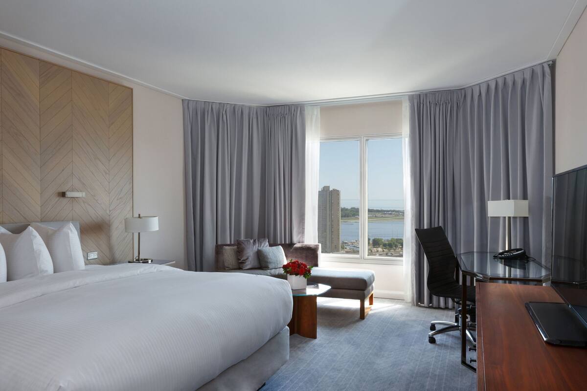 A hotel room with a large bed, a desk, a chair, and a view of the city.