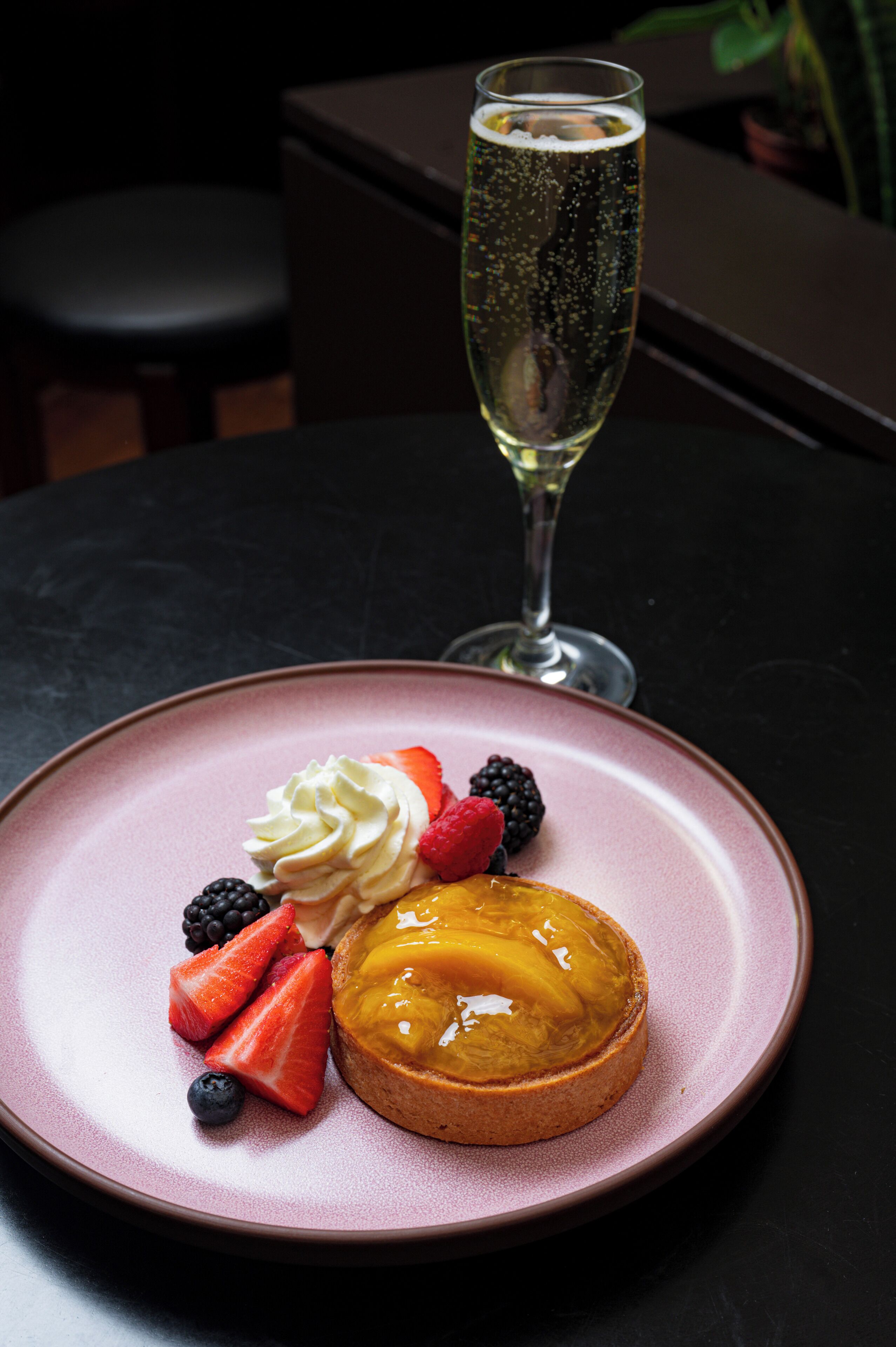 A dessert plate with a pastry, fruit, and a glass of champagne on a table.