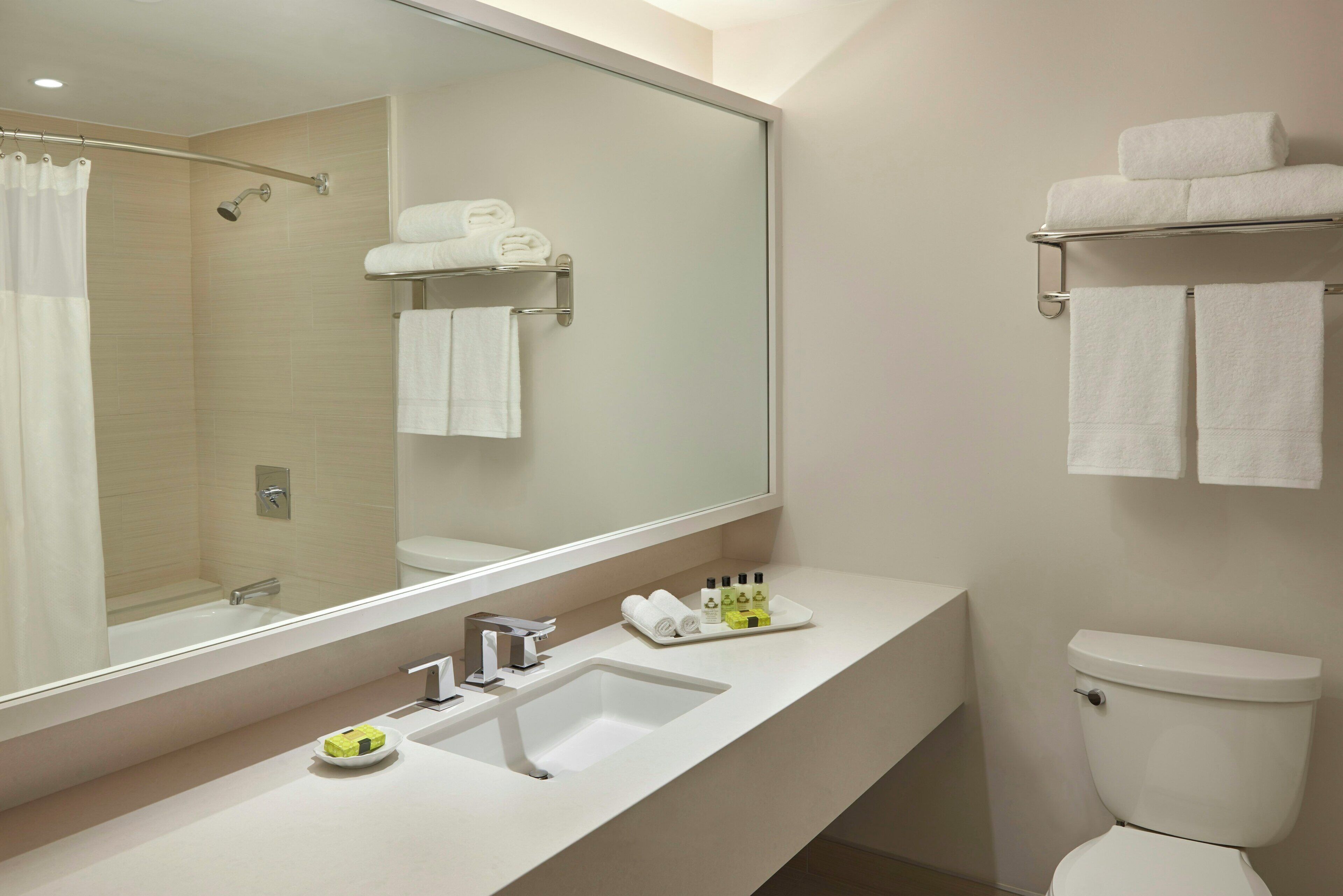 Ein modernes Badezimmer mit großem Spiegel, Waschbecken, Toilette und Duschbereich.