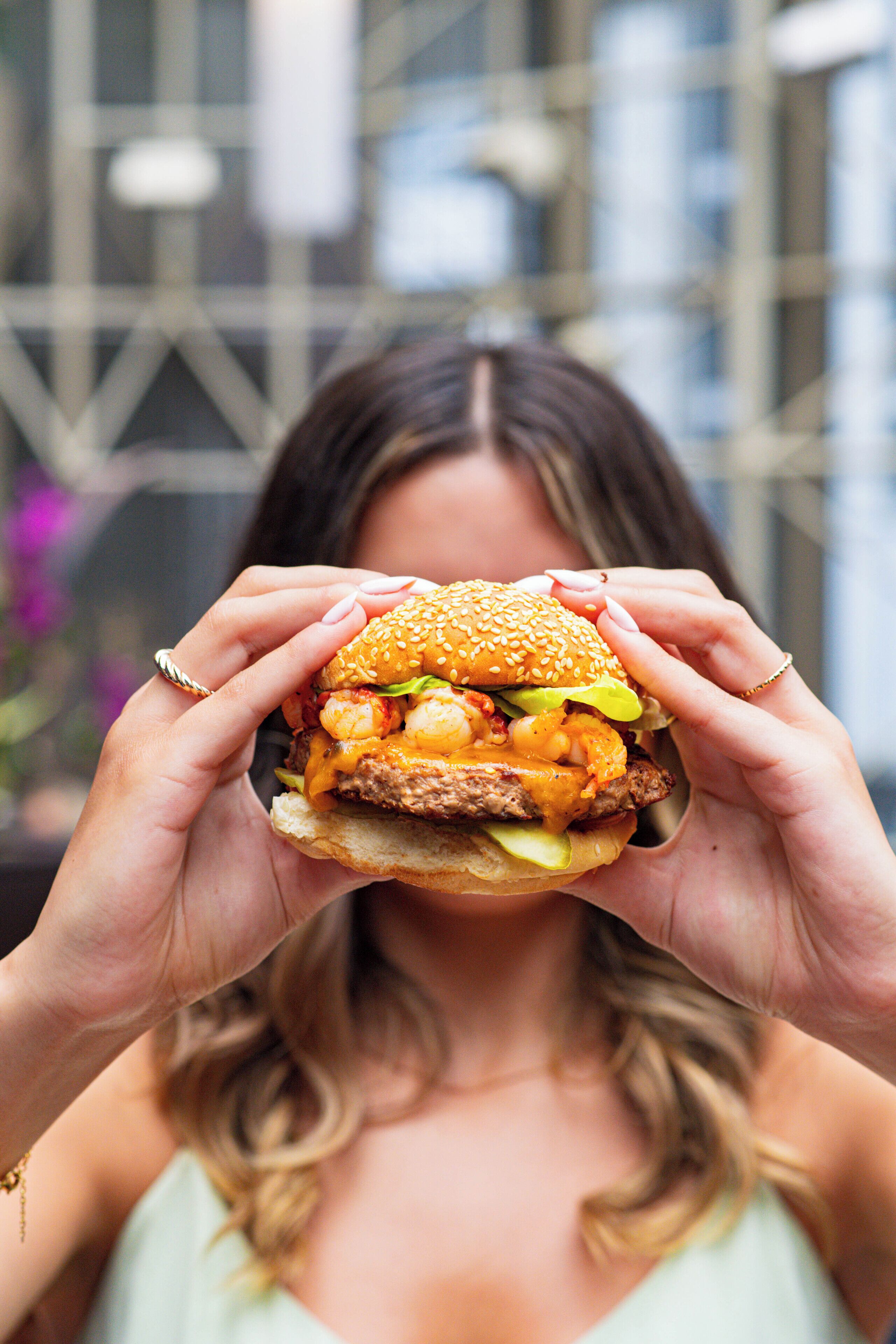 Een persoon houdt een hamburger vast, met zichtbare ingrediënten zoals sla, kaas en een sesamzaadbolletje.