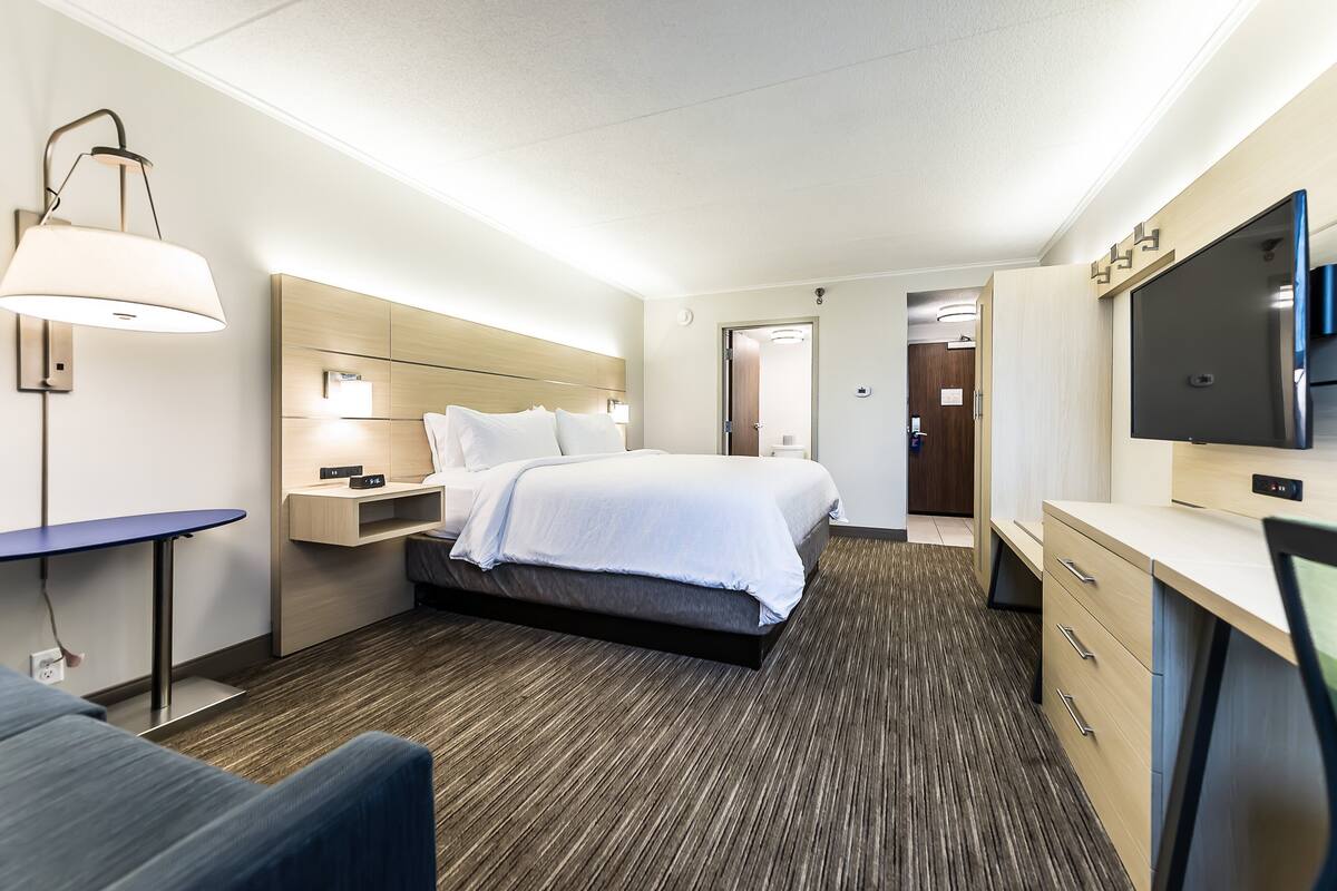 Une chambre d’hôtel comprenant un lit, une table de chevet, une lampe, une télévision et un bureau avec des tiroirs.