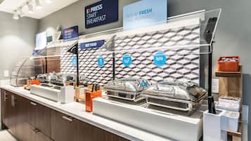 Un espace buffet avec des sections clairement indiquées pour le petit-déjeuner et les plats chauds, ainsi qu’un panneau demandant aux clients s’ils se sentent en forme.