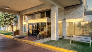 A modern building with a covered entrance, stone pillars, and a bench outside. - Holiday Inn Express Flint-Campus Area by IHG (Flint)