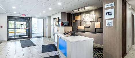 A hotel reception area with a check-in counter, a digital screen, and a sign indicating check-in times.