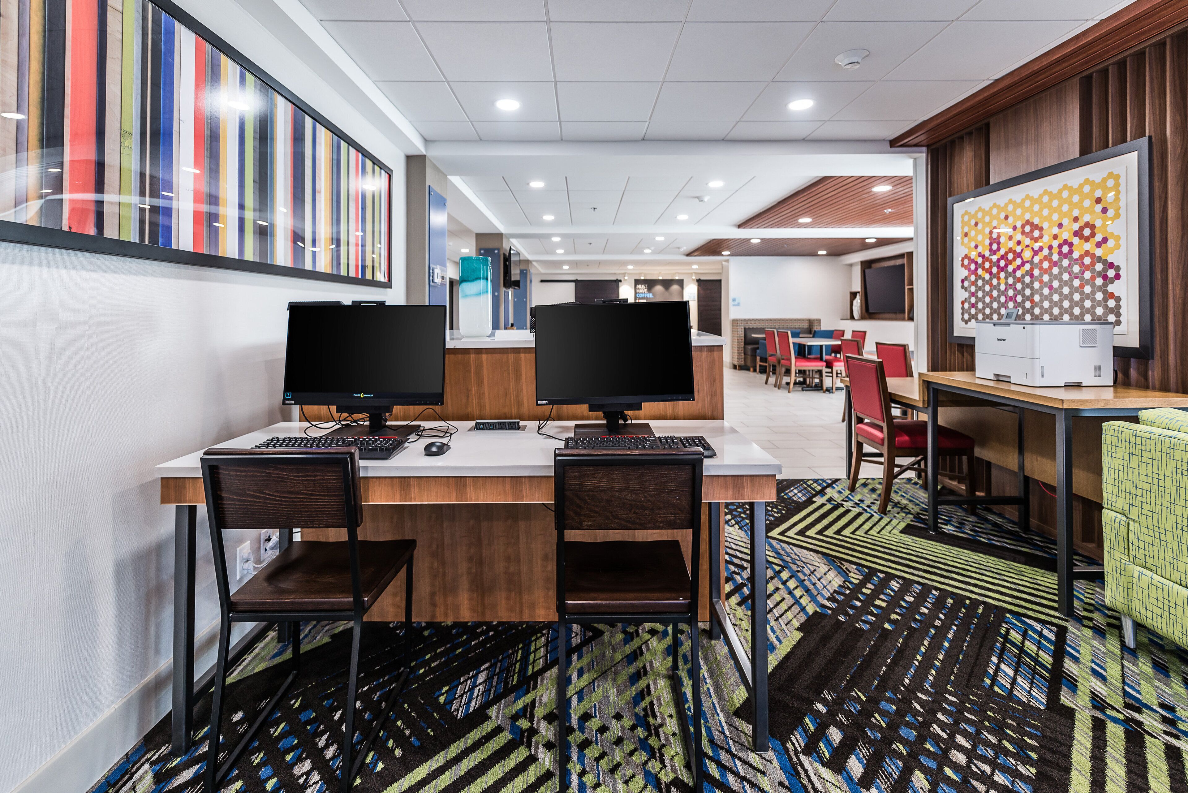 A modern conference room with two desks, each with a computer and chair, a large screen, and a patterned carpet.