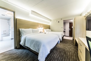 A hotel room with two beds, a wooden headboard, a desk with drawers, and a bathroom visible through an open door.