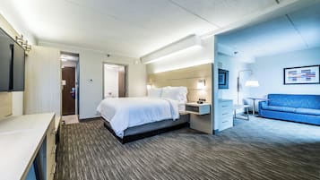 A hotel room with a bed, bedside table, desk, and a blue sofa.