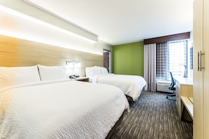 A hotel room with two beds, a desk, and a window with curtains.