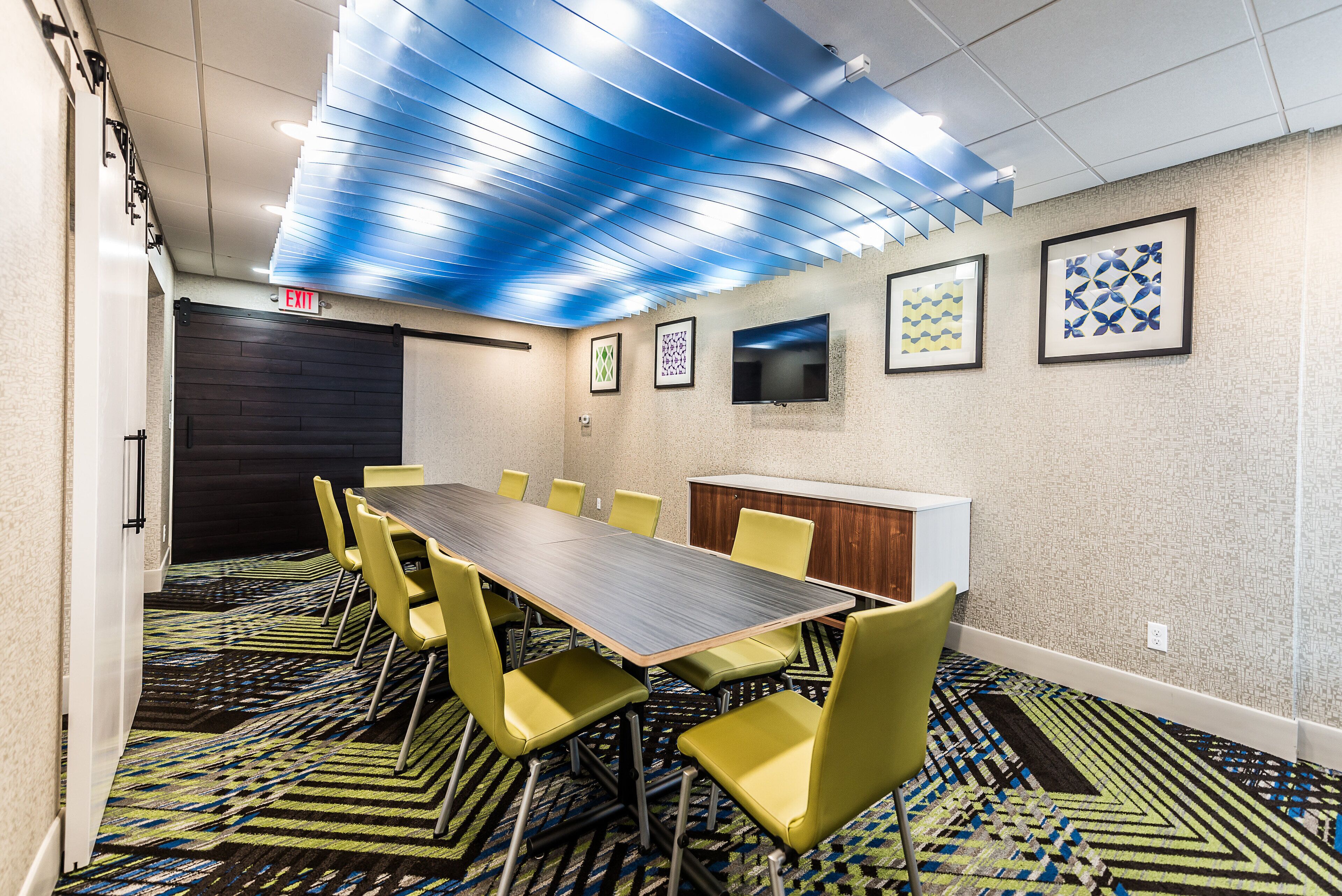 A conference room with a long table, yellow chairs, patterned carpet, and framed artwork on the walls.