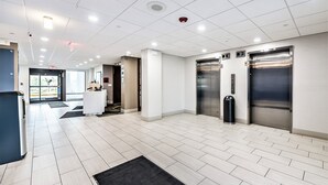 A modern lobby with a reception desk, two elevators, and a trash bin. - Holiday Inn Express Flint-Campus Area by IHG (Flint)