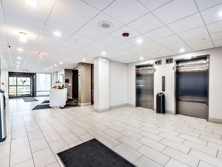 A modern lobby with a reception desk, two elevators, and a trash bin.