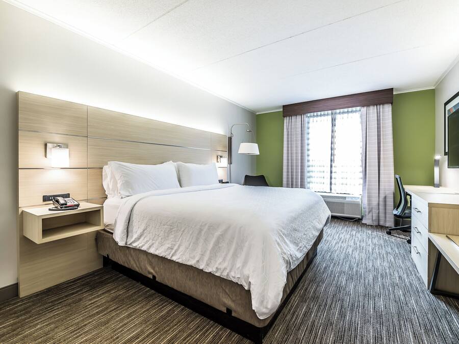 A hotel room with a bed, bedside table, lamp, desk, chair, and a television.