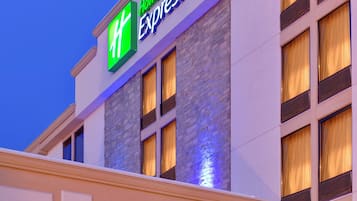 A Holiday Inn Express hotel with a prominent green and white sign, multiple windows with curtains, and a stone facade.