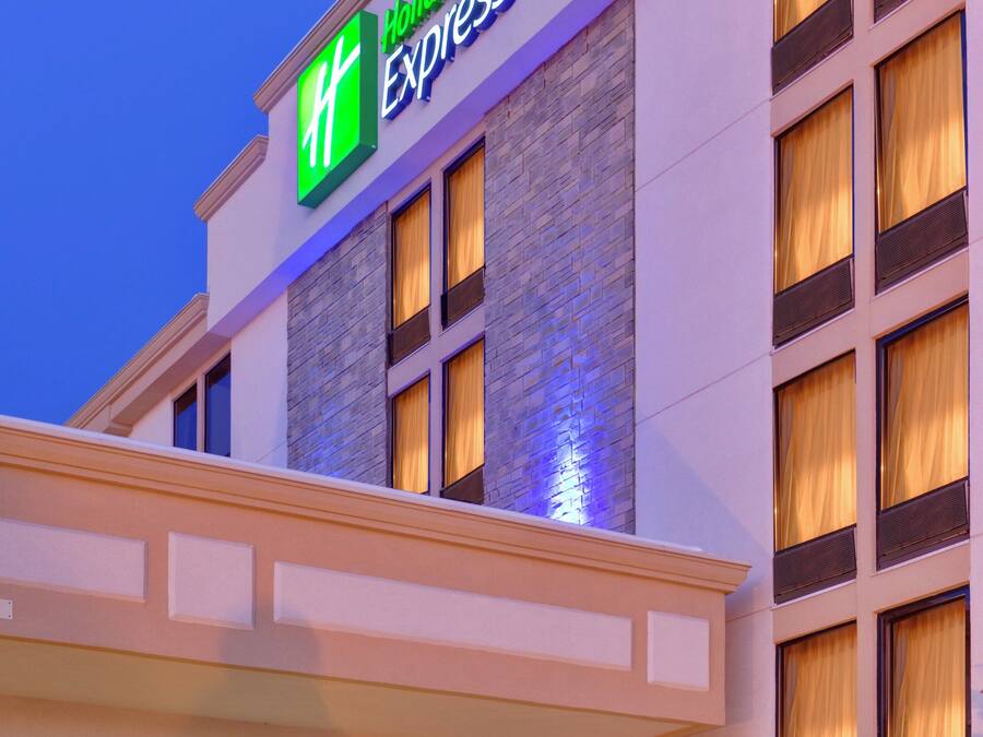 Um hotel Holiday Inn Express com uma placa verde e branca bem visível, várias janelas com cortinas e fachada de pedra.