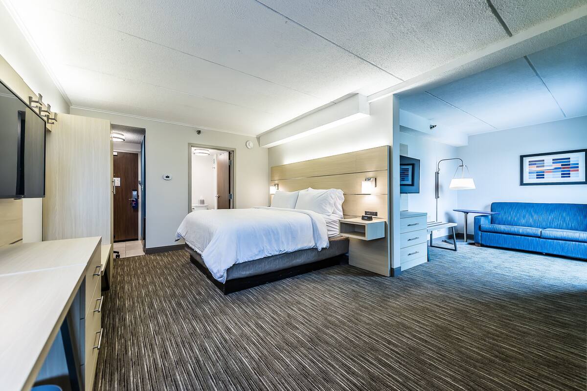 Une chambre d’hôtel avec un lit, une table de chevet, un bureau et un canapé bleu.