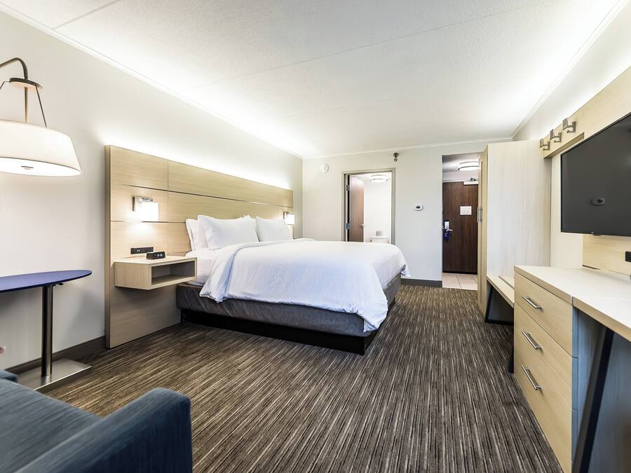 A hotel room with a bed, bedside table, lamp, TV, desk, and a chair.