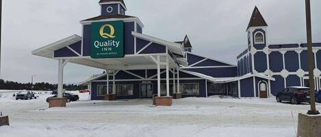 A Quality Inn by Choice Hotels with a distinctive blue and white color scheme, a covered entrance, and a snow-covered parking lot.
