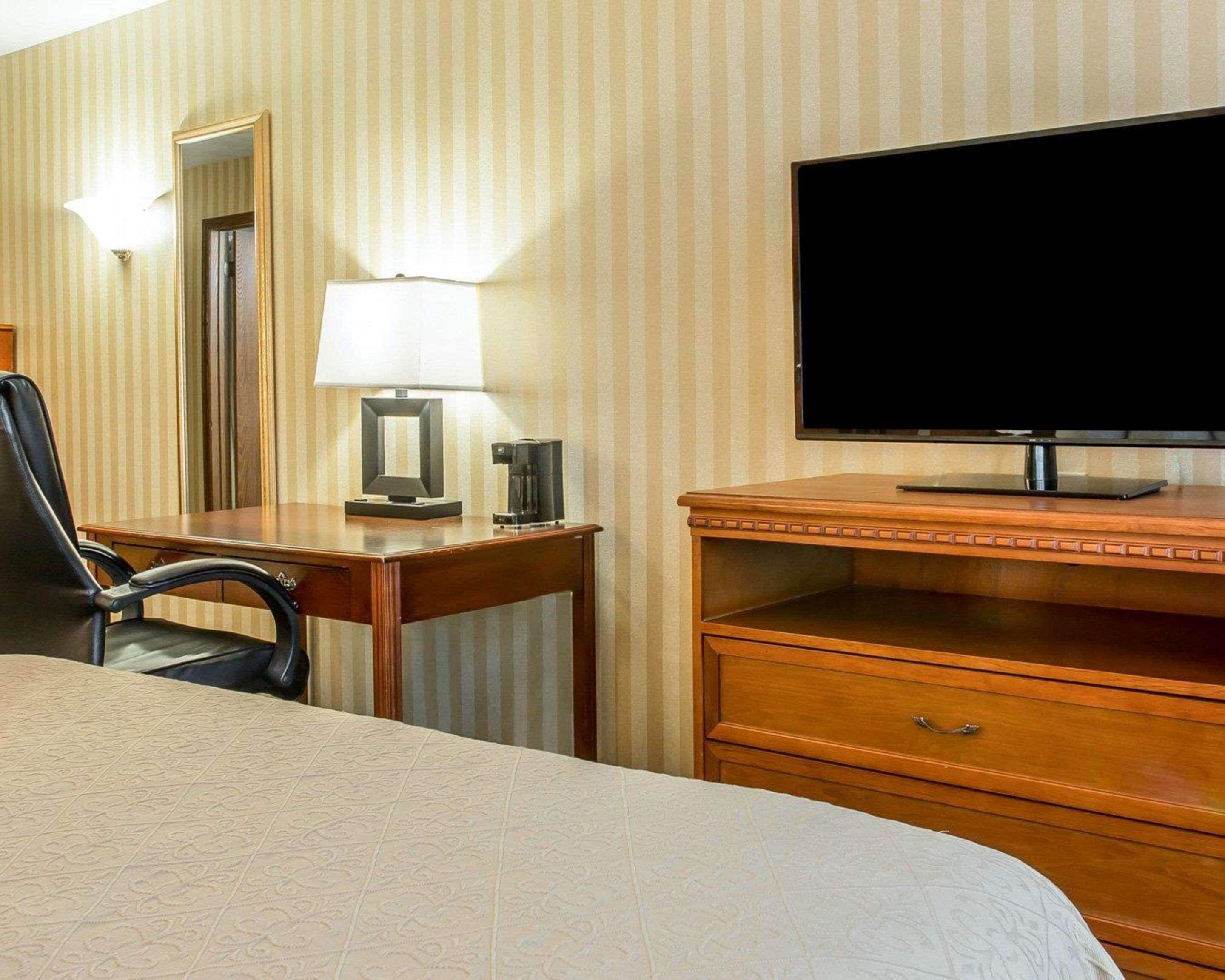 A hotel room with a bed, a desk with a lamp, a coffee maker, a TV, and a dresser.