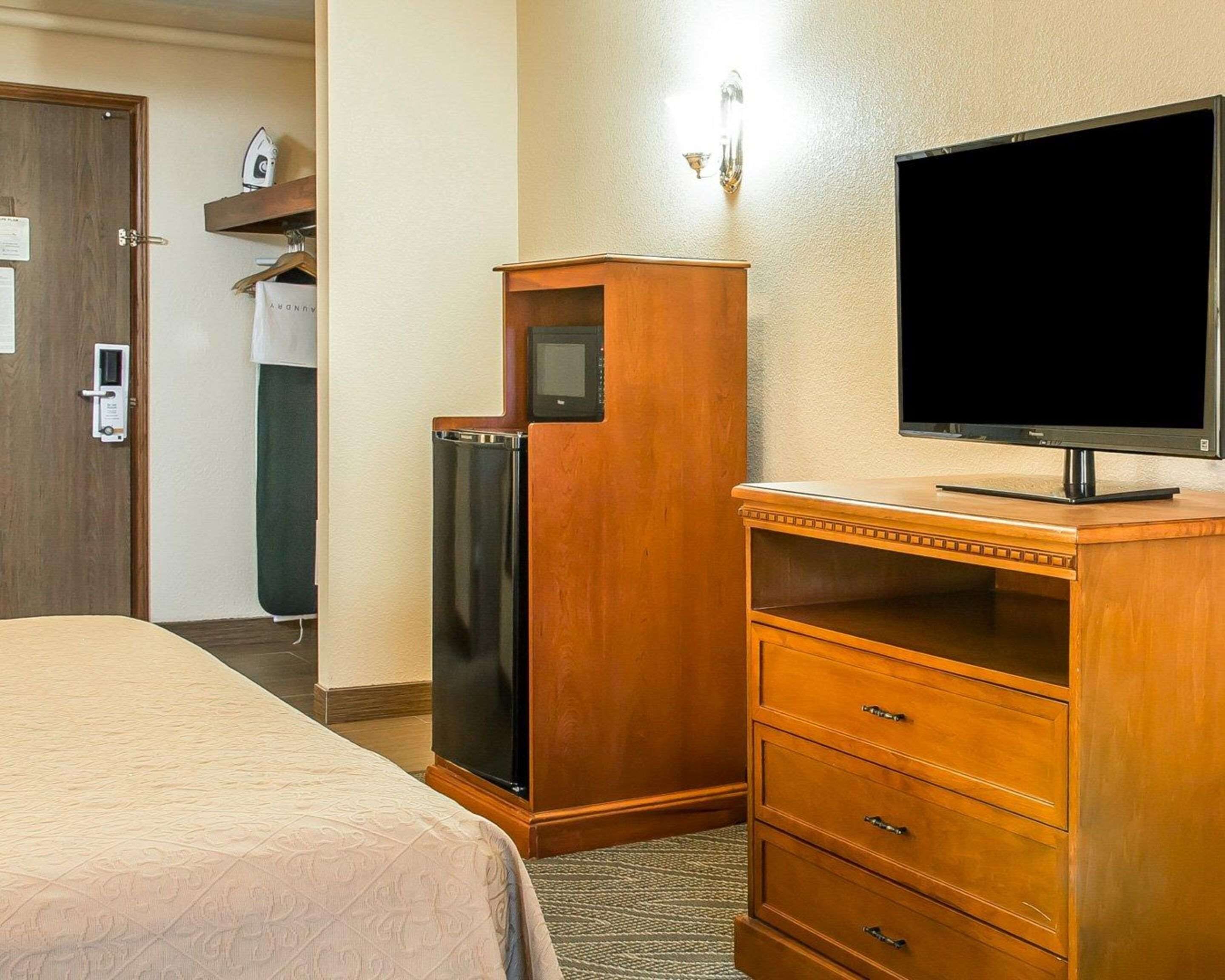 A hotel room with a bed, a wooden dresser with a flat-screen TV, a refrigerator, and a door with a lock.