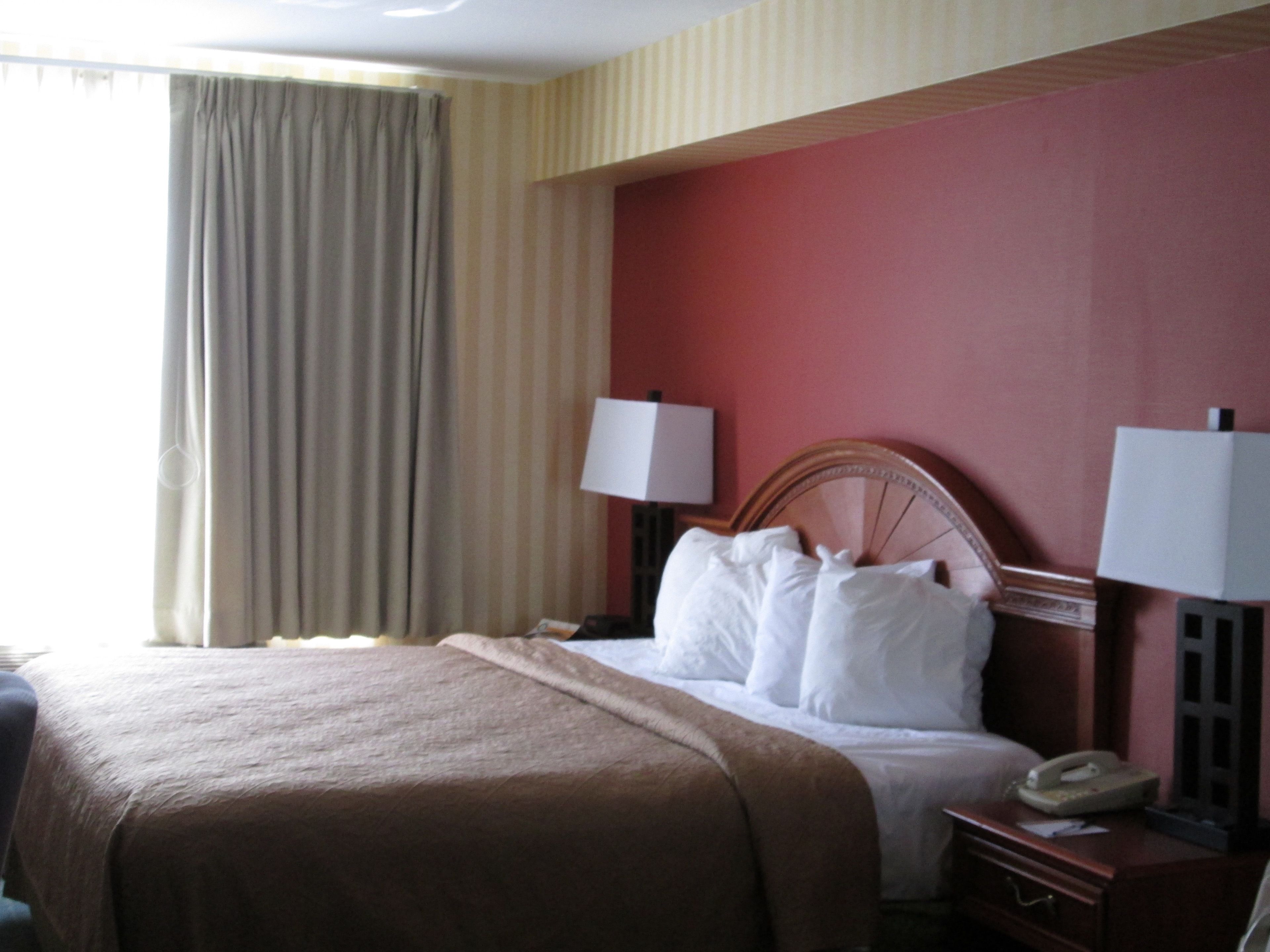 A hotel room with a bed, a nightstand, a lamp, a telephone, and a window with curtains.