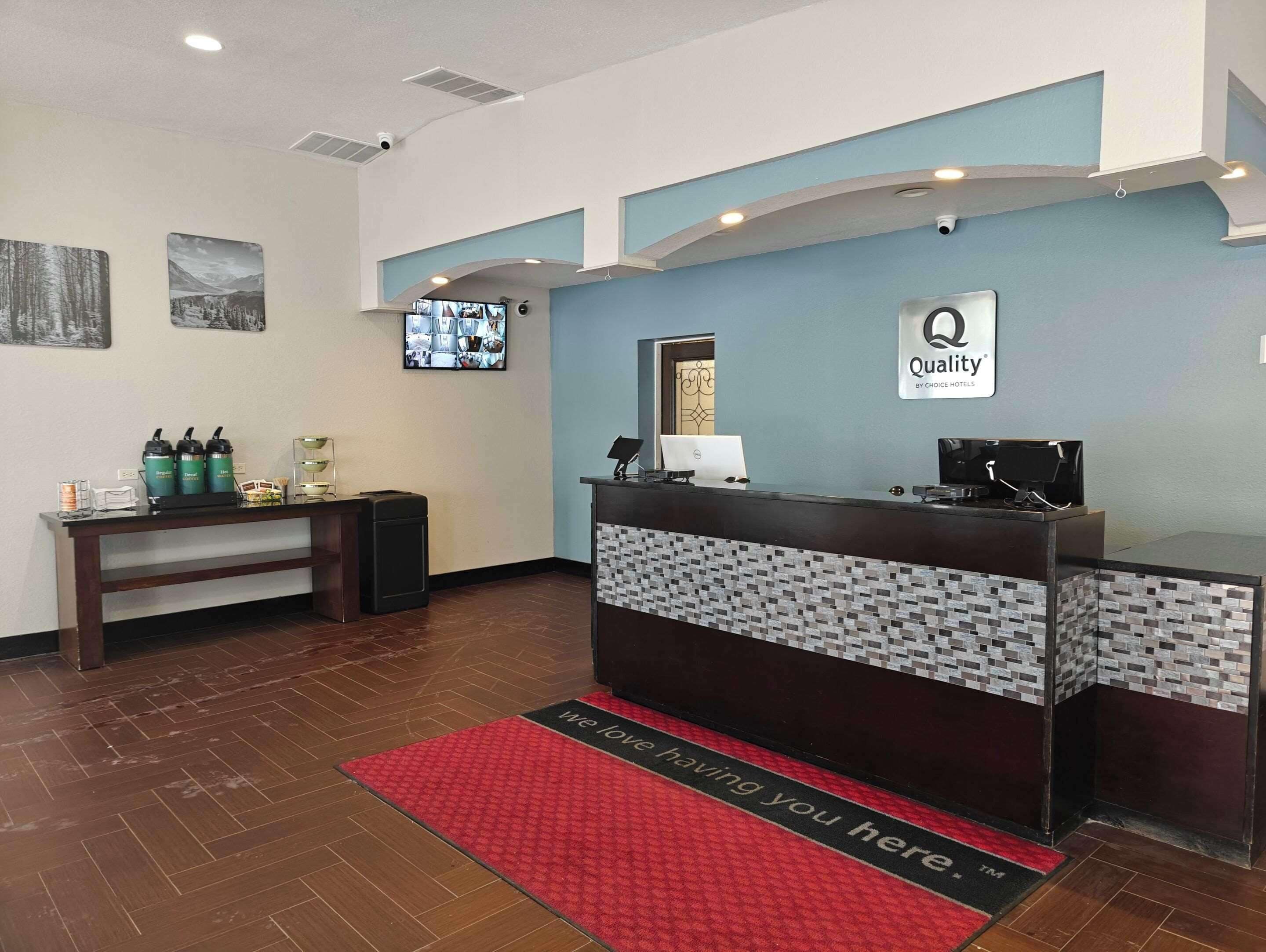 A hotel reception area with a reception desk, a mounted television, and a coffee station.