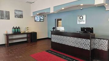 A hotel reception area with a reception desk, a mounted television, and a coffee station.