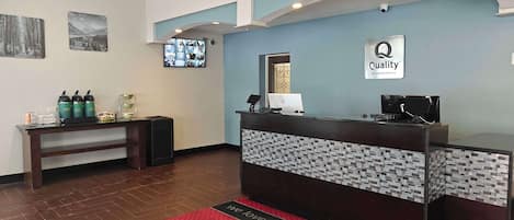 A hotel reception area with a reception desk, a mounted television, and a coffee station.