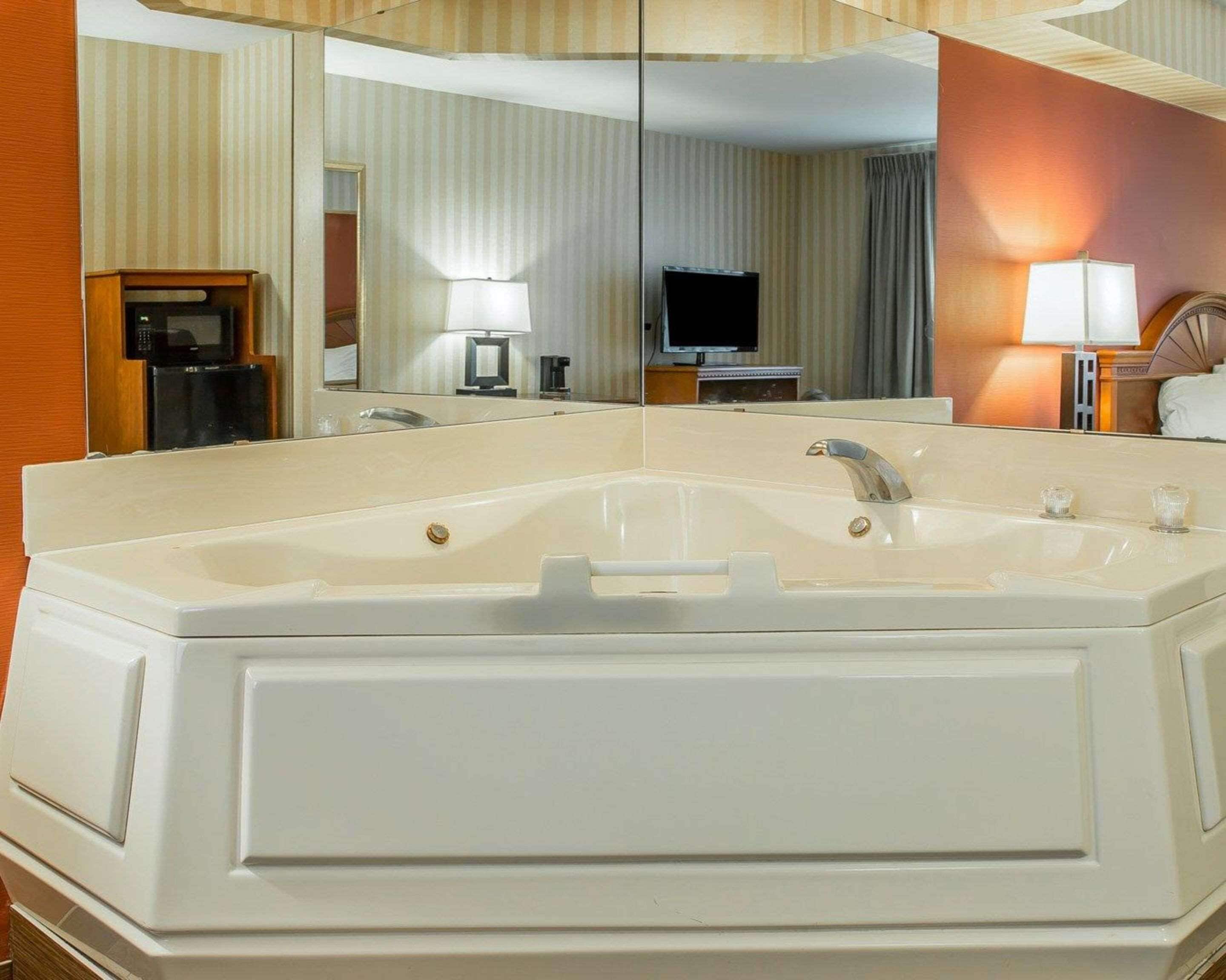 A large, white bathtub with a single faucet and a handheld showerhead, a mirror above it, and a television in the background.