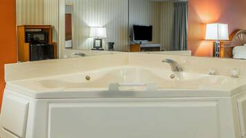 A large, white bathtub with a single faucet and a handheld showerhead, a mirror above it, and a television in the background.