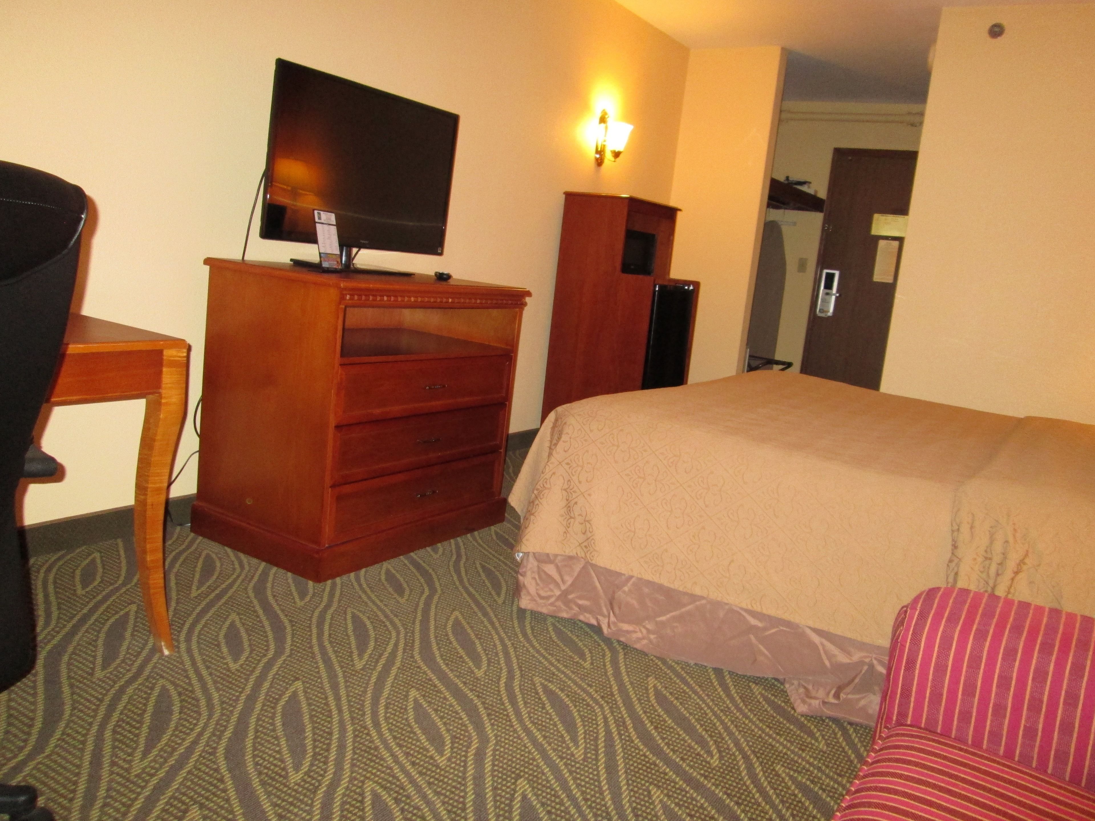 Ein Hotelzimmer mit einem Bett, einem Schreibtisch mit Fernseher, einem Schminktisch und einer Wandleuchte.
