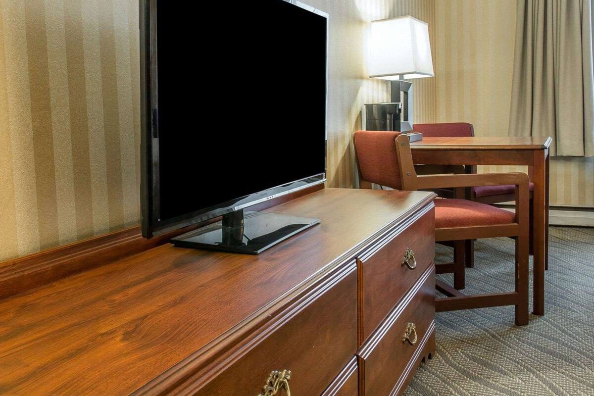 Una camera d'albergo con una scrivania in legno, una televisione, una lampada e una sedia.