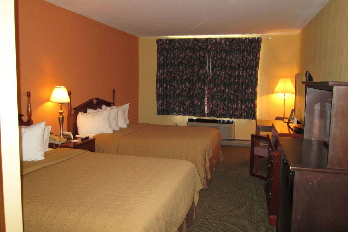 Ett hotellrum med två sängar, ett skrivbord, en tv och ett fönster med blommiga gardiner.