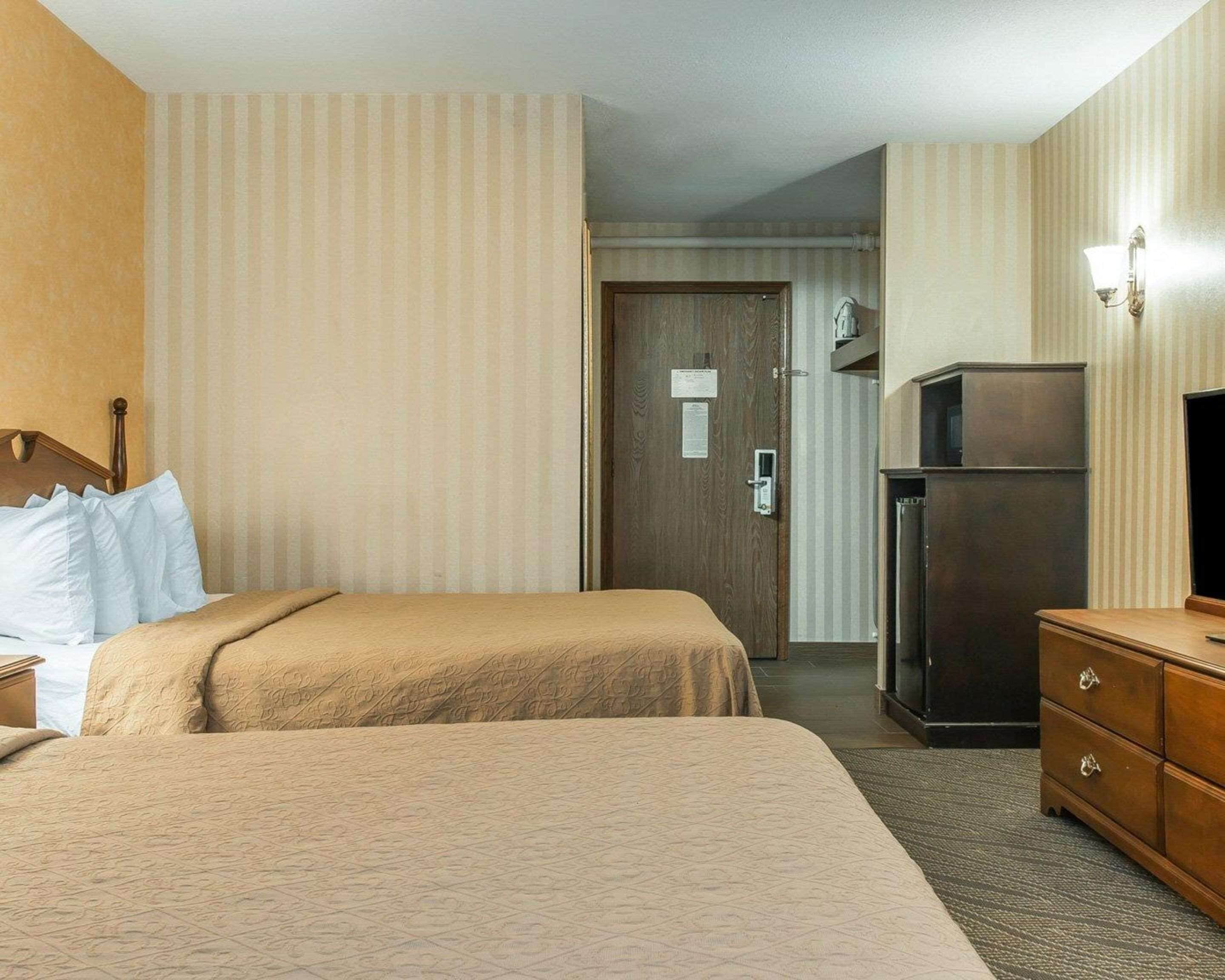 A hotel room with two beds, a refrigerator, a dresser, and a door leading to another room.
