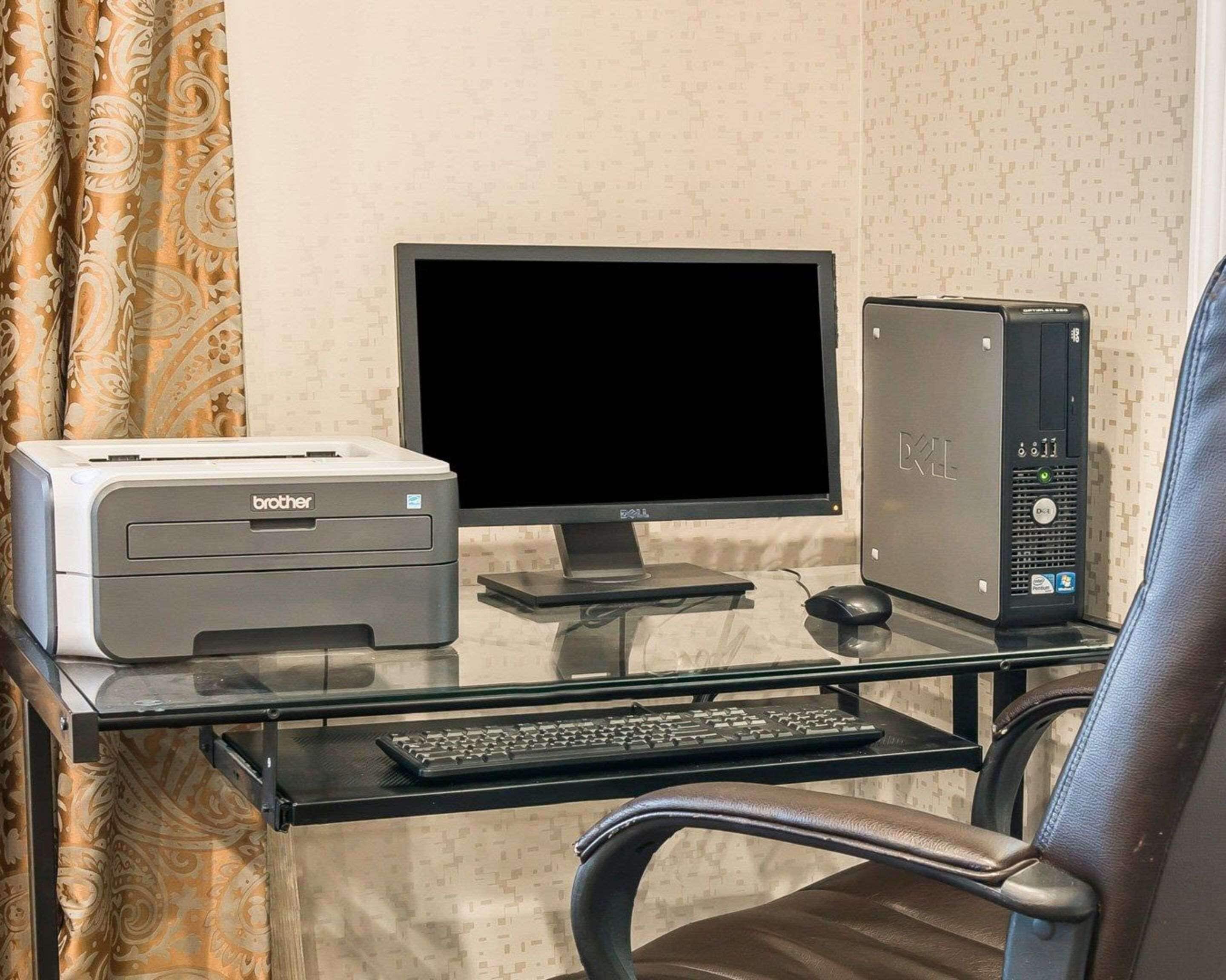 A home office setup with a Brother printer, a Dell monitor, and a desktop computer on a glass desk.