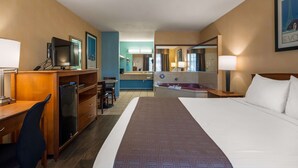 Quarto de hotel com cama, escrivaninha, televisão e banheiro com banheira.