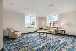 Habitación de hotel con alfombra estampada, un sofá, una silla y dos lámparas.
