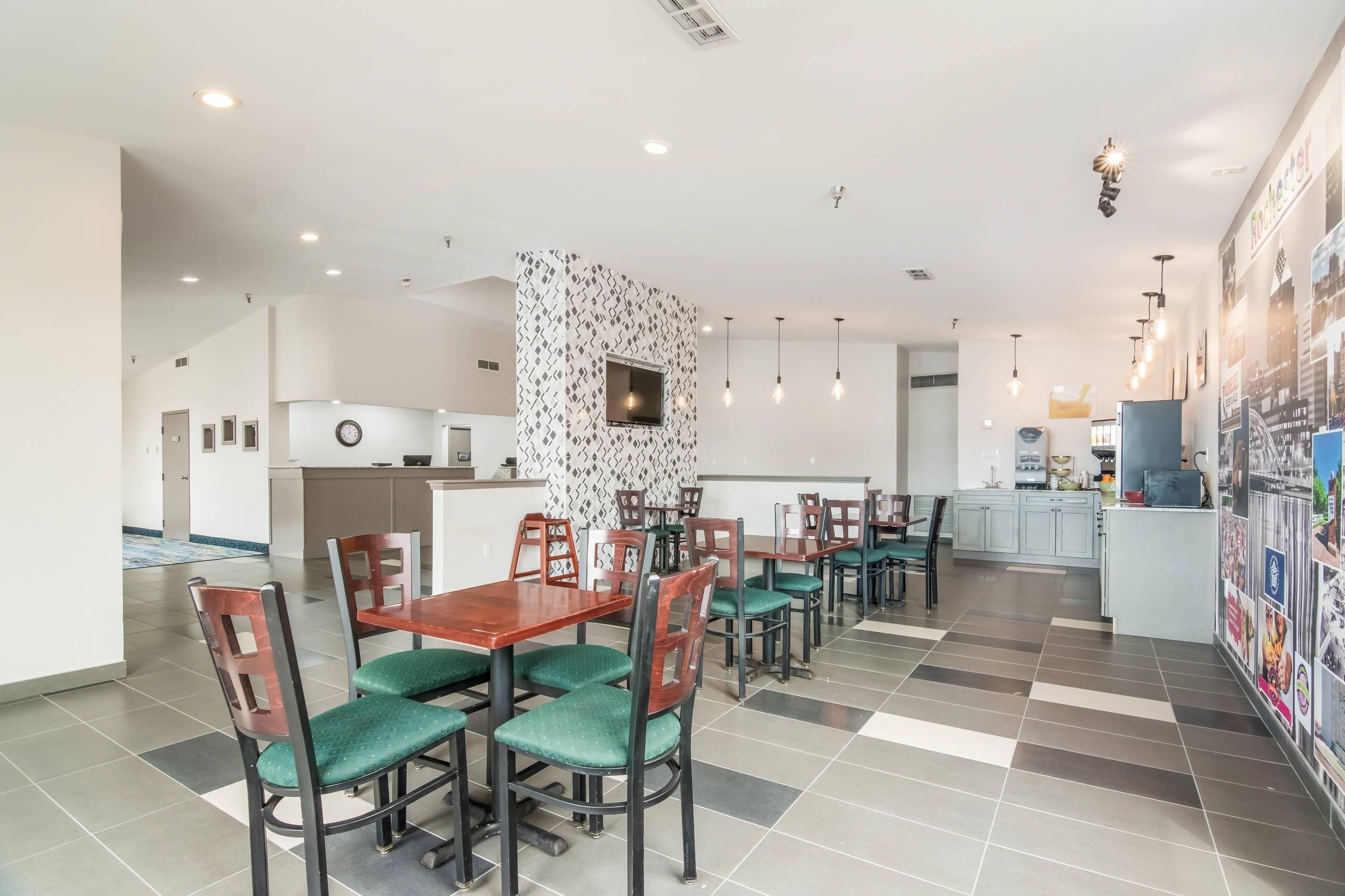 Une salle à manger d’hôtel avec plusieurs tables et chaises, une cuisine à l’arrière-plan et un mur orné d’un motif décoratif.